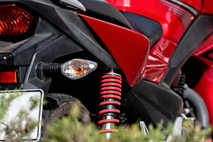 Vista de un amortiguador trasero instalado en una motocicleta roja, parte del sistema de suspensión.