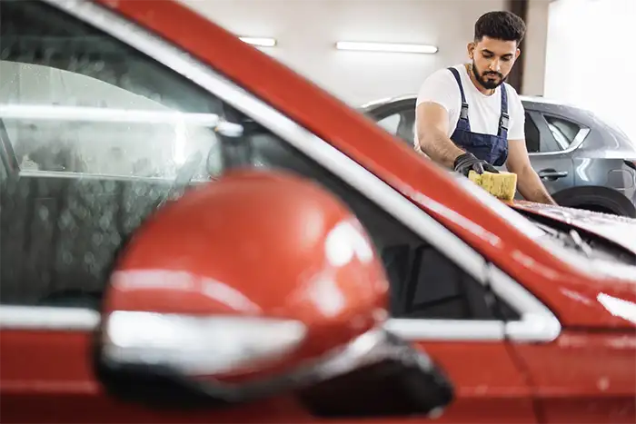 Mecánico trabajando en la limpieza y pulido de la carrocería de un automóvil rojo en el taller.