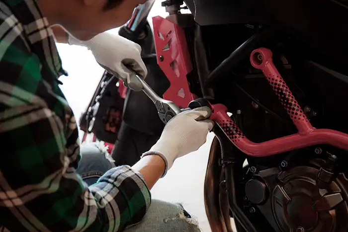 Mecánico ajustando piezas en una motocicleta durante un proceso de reparación.